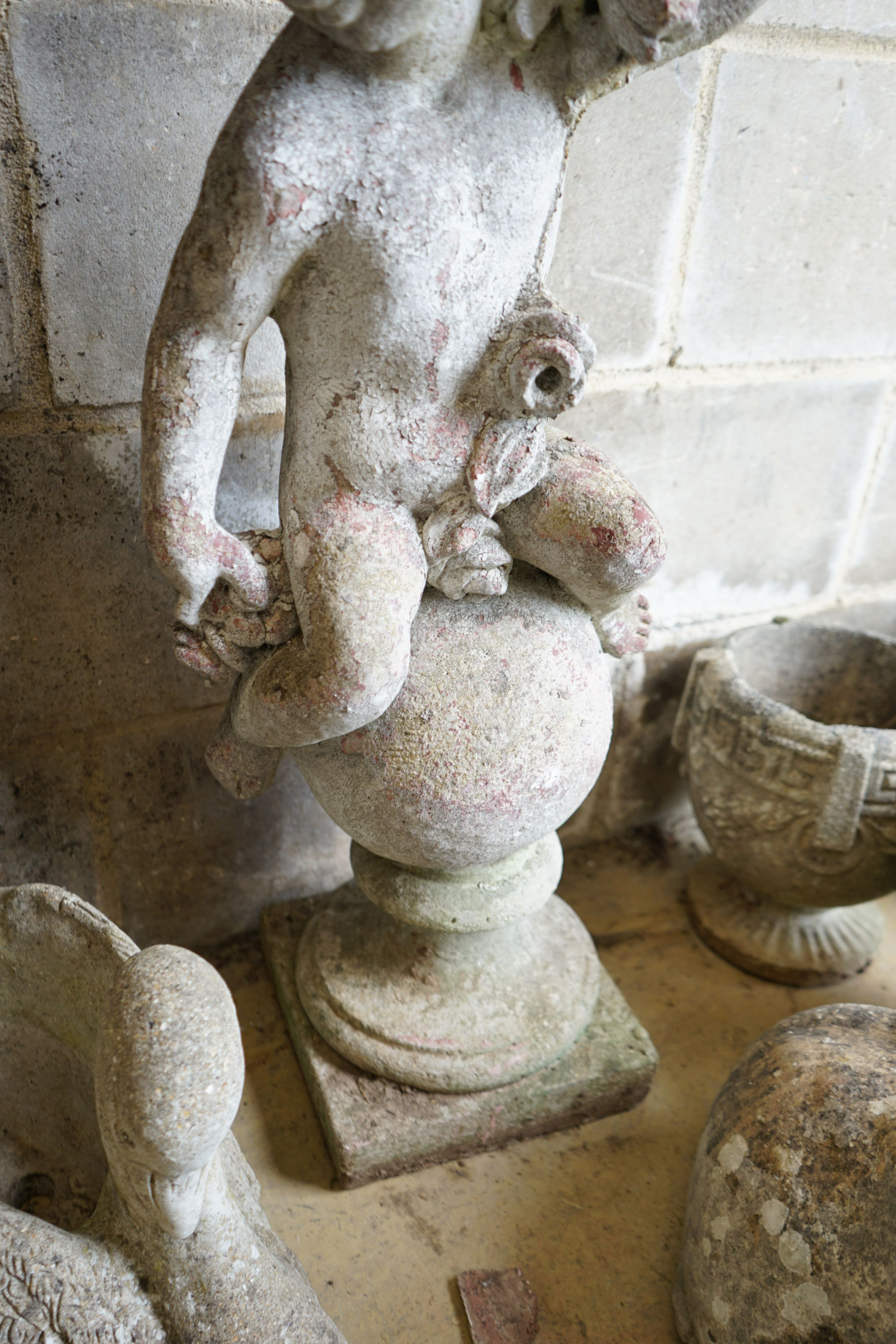 A reconstituted stone seated cherub and orb garden ornament, height 84cm